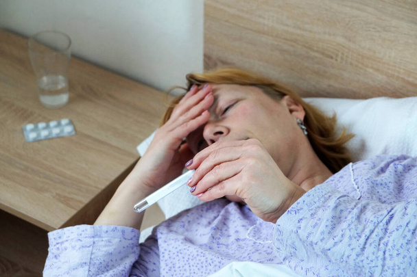 eine kranke Frau liegt im Bett und blickt auf ein Thermometer. - Foto, Bild