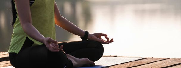 Joven asiática hermosa mujer practicando yoga y meditar en la pose de loto al aire libre junto al lago en la mañana para la relajación y la paz de la mente. Concepto de armonía y meditación. Estilo de vida saludable - Foto, Imagen