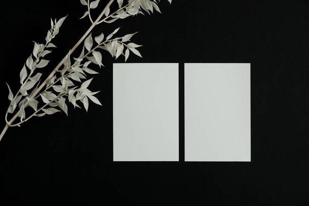 Scheda foglio di carta bianca con spazio copia mockup e ramo floreale asciutto su sfondo nero. Modello minimale di marchio di business estetico. Posa piatta, vista dall'alto - Foto, immagini