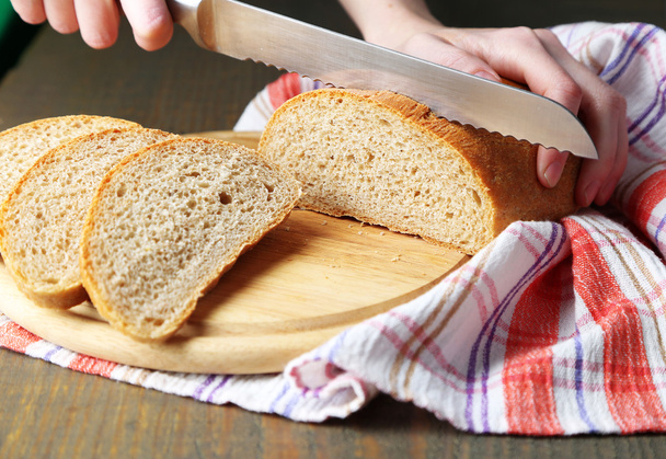 Female hands cutting bread on wooden board, close-up - 写真・画像