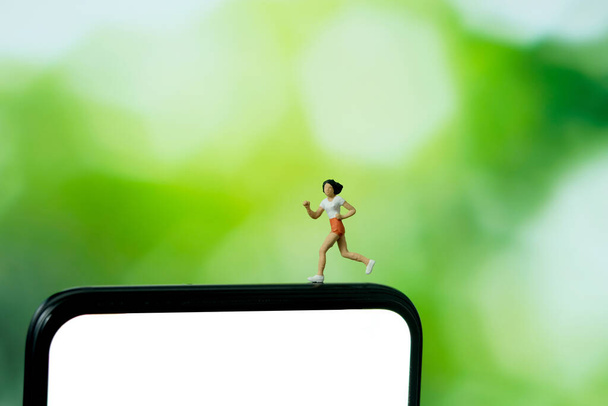 Correr y trotar concepto de aplicación de seguimiento. Un hombre corriendo por encima del smartphone. Personajes en miniatura fotografía. - Foto, imagen
