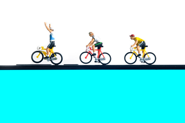 Trenażer rowerowy i aplikacja śledząca. Jazda na rowerze nad smartfonem. Miniaturowi ludzie figurują fotografię konceptualną. - Zdjęcie, obraz