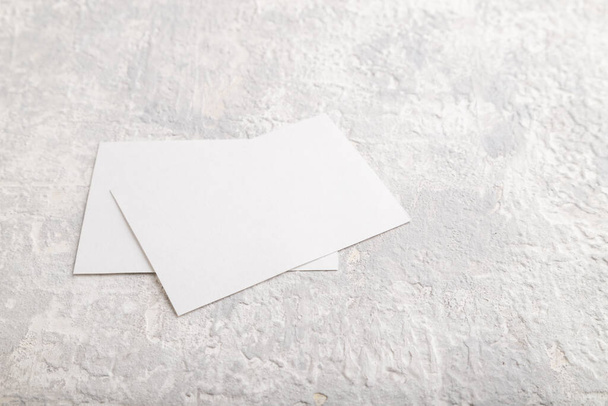 Tarjeta de visita de papel blanco, maqueta sobre fondo de hormigón gris. En blanco, vista lateral, naturaleza muerta, espacio para copiar. - Foto, Imagen