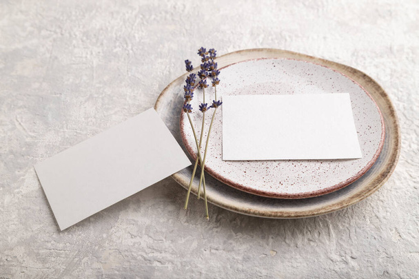 White paper invitation card, mockup with lavender on ceramic plate and gray concrete background. Blank, side view, still life, copy space. - Photo, Image