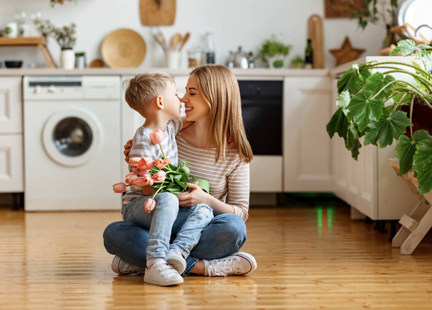 Люблячий маленький син обіймає щасливу маму і вітає з букетом тюльпанів під час святкування Дня матері вдома
 - Фото, зображення