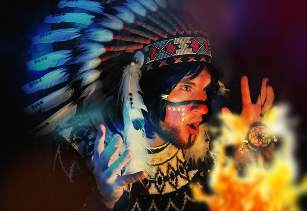 Portret młodego przystojniaka w kapeluszu z piórem wodza Indian. Ogień i człowiek - portret - Zdjęcie, obraz