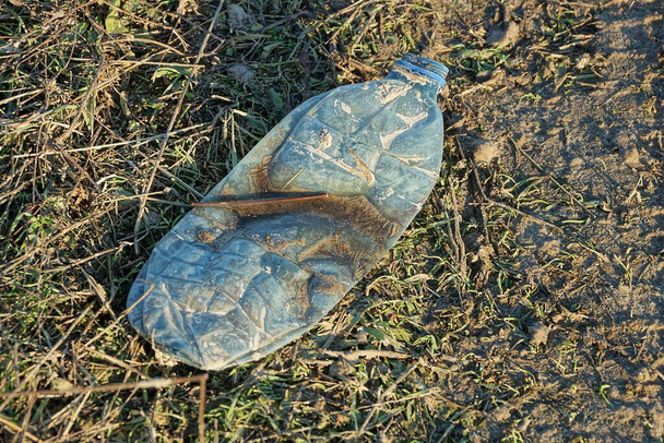 odpadky z jedné špinavé modré plastové láhve leží na trávě a zemi venku - Fotografie, Obrázek