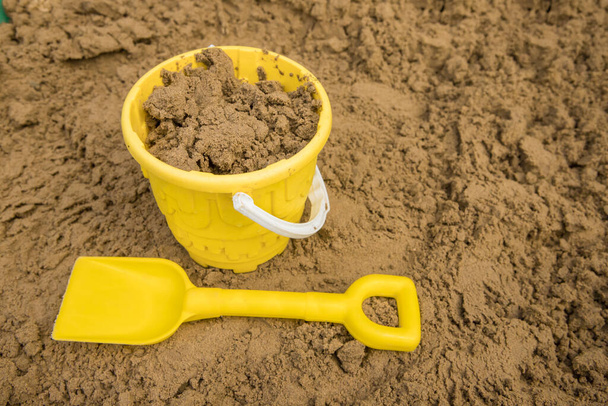 Żółte wiadro i łopata w piasku, gotowe do robienia zamków z piasku w słońcu - Zdjęcie, obraz