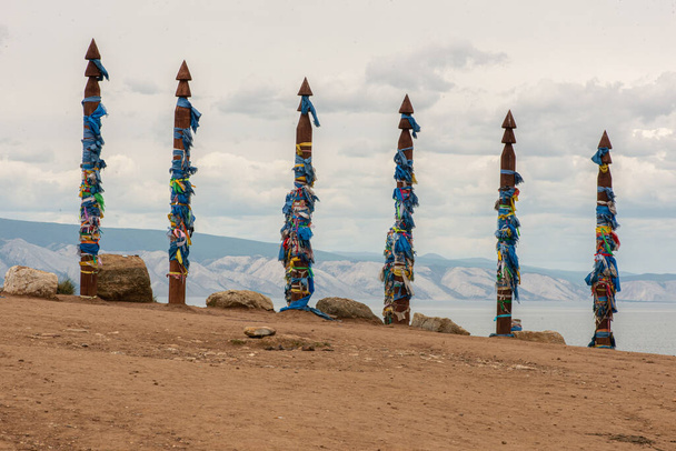 Een serie serges in Shamanka op Olkhon Island. Rij van 6 hoge rituele Buryat religieuze pilaren gebonden met gekleurde linten, tegen de achtergrond blauwe lucht met wolken. - Foto, afbeelding
