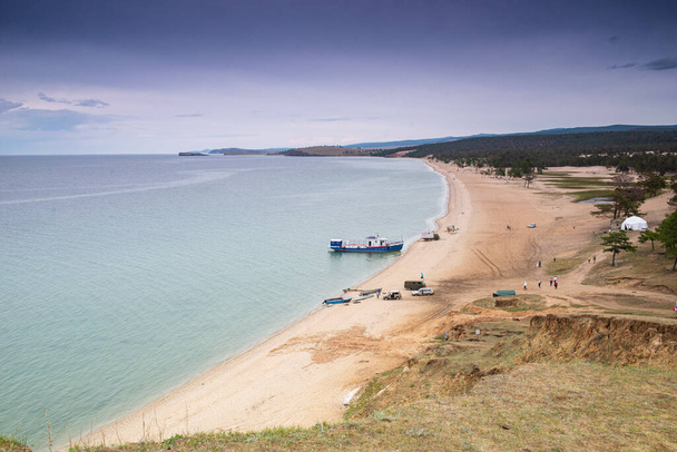 Sandy coast of Lake Baikal. A tourist ship is visible in the background. Blue sky and sandy beach, beautiful clouds. Khuzhir is the main village on Olkhon Island in eastern Siberia. The photo was taken in the summer in July. - Photo, Image