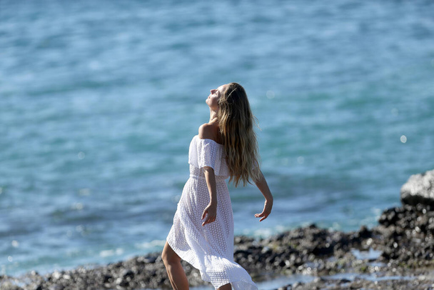 Dziewczyna w białym ubraniu boso spaceruje i pozuje po skalistym morzu  - Zdjęcie, obraz