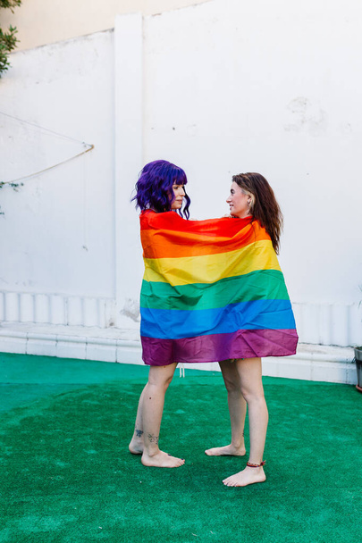 Duas mulheres com bandeira de arco-íris num quintal. Casal Meninas lésbicas jovens segurando uma bandeira do arco-íris e abraçando alegremente. Um par de mulheres lésbicas - Foto, Imagem