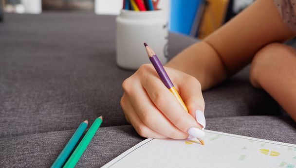 Dívka dělá zbarvení s multi-barevné tužky, zblízka na ruce. Domácí umělecký koníček. - Fotografie, Obrázek