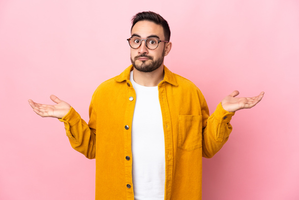 Young caucasian handsome man isolated on pink background having doubts while raising hands - Photo, Image