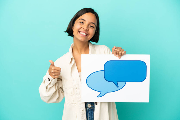 Young mixed race woman isolated on blue background holding a placard with speech bubble icon with thumb up - Foto, Bild