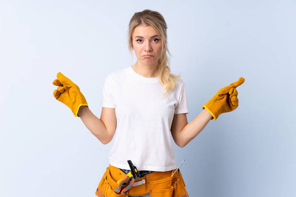 Electrician woman over isolated blue background pointing to the laterals having doubts - Photo, image