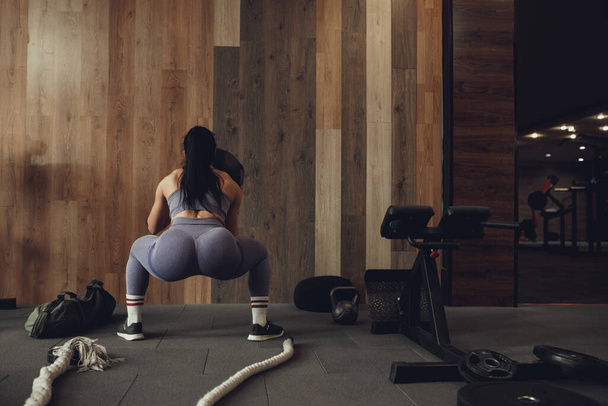 A girl athlete with a pumped-up booty squats with a phyto ball near the wall - Photo, Image