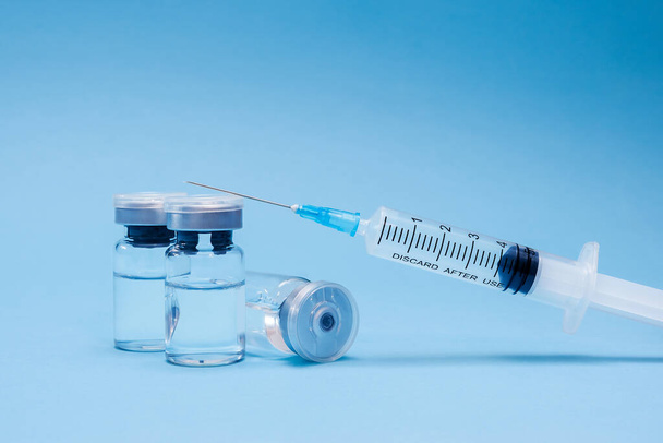 Ампула, флакон, шприц на синем фоне. Концепция вакцинации, профилактика заболеваний. Здравоохранение, разработка коронавирусной вакцины - Фото, изображение