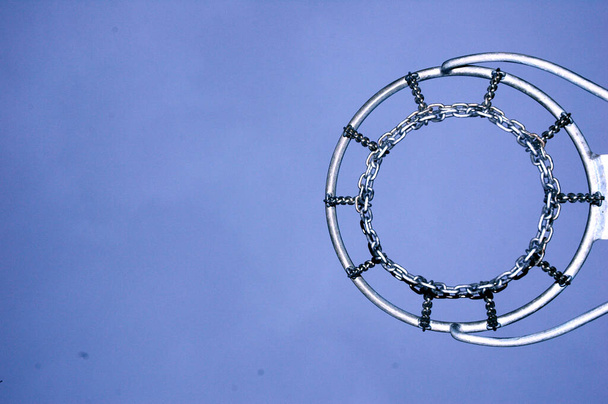 Одинокое баскетбольное кольцо с блестящей металлической сеткой на открытой игровой площадке ночью снизу - Фото, изображение