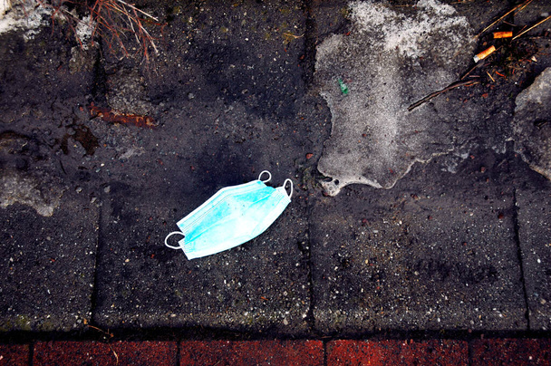 Máscara cirúrgica azul usada contra corona covid 19 jogado na rua cercado por sujeira e sujeira - Foto, Imagem