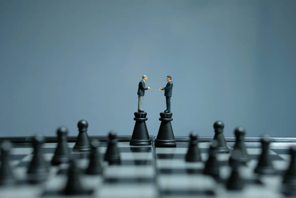 Business strategy conceptual photo - Two miniature businessman make handshake partnership agreement above castle pawn on a chessboard - Photo, Image