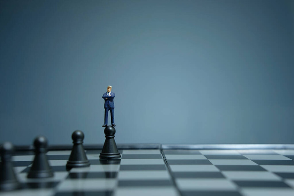 Business strategy conceptual photo - miniature businessman standing above castle pawn on a chessboard - Photo, Image
