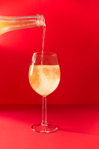Lesklé šampaňské nalévající se do skla na červeném pozadí. Nový rok, Vánoce, Valentýn, Den žen nebo Den matek sváteční přání s copyspace - Fotografie, Obrázek