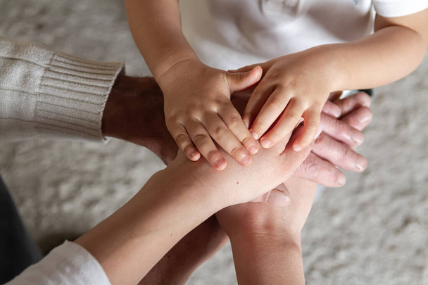 Grandfather, his daughter and little grandson together make a stack of palms and hands. Happy family togetherness. Happy family and support for elderly parents concept. - Photo, Image