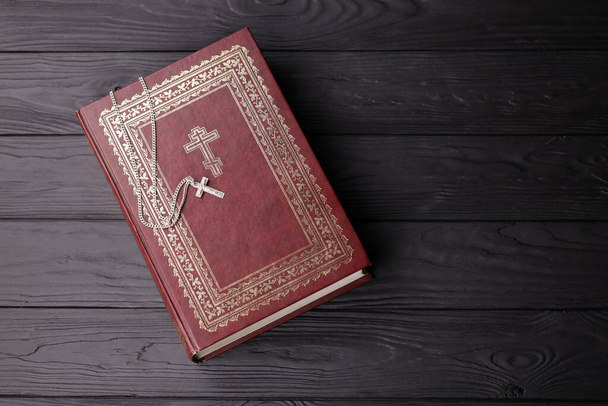 Ασημένιο κολιέ με σταυρό στο βιβλίο της Αγίας Γραφής σε μαύρο ξύλινο τραπέζι. Ζητώντας ευλογίες από τον Θεό με τη δύναμη της αγιότητας, η οποία φέρνει τύχη και δείχνει συγχώρεση. - Φωτογραφία, εικόνα