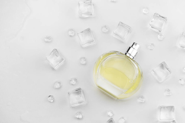 Vrouwelijke parfum gele fles, Objectieve foto van parfum fles in ijsblokjes en water op witte tafel. Zicht van bovenaf. Mockup product foto, concept van versheid en aroma - Foto, afbeelding