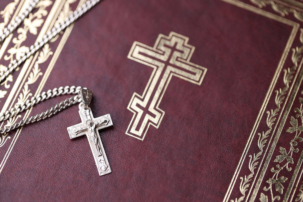 Ezüst nyaklánc kereszt kereszttel a keresztény szent biblia könyvön, fekete fa asztalon. Áldást kérni Istentől a szentség erejével, ami szerencsét hoz és megbocsátást mutat.. - Fotó, kép