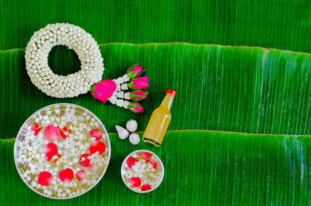 Songkran festival background with jasmine garland, flowers in water bowls, scented water and marly limestone for blessing on wet banana leaf background. - Photo, Image
