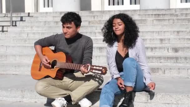 Ένα νεαρό ζευγάρι Λατίνων να παίζει κιθάρα και να τραγουδάει στις σκάλες. Χιλιετής γενιά. - Πλάνα, βίντεο