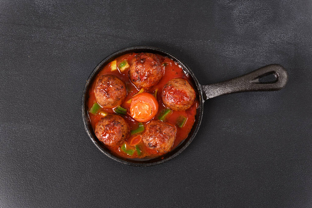 Тушеные фрикадельки в томатном соусе в кастрюле на темном фоне. - Фото, изображение