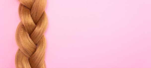 Braid vaaleanruskea keinotekoisia hiuksia vaaleanpunainen tausta, vapaata tilaa tekstiä. Käsite kampaamo, hiusten pidennykset. - Valokuva, kuva