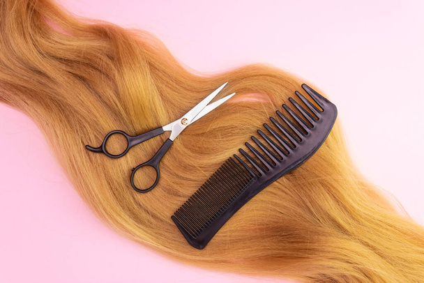 Red artificial hair on a pink background, comb and scissors. The concept of hairstyle, haircut, hair care. - Photo, Image