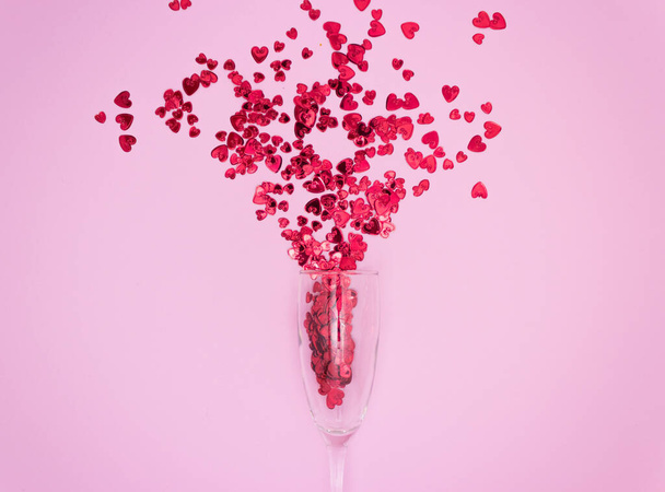Красные сердца вытекают из бокала шампанского. Розовый фон, вид сверху. - Фото, изображение