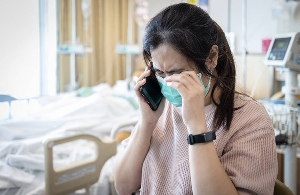 Sad asian woman using cell phone to tell relative bad news,stressed worried about worsening health after surgery,grieving crying in the intensive care,waiting for her mother to recover in the ICU room - Photo, Image