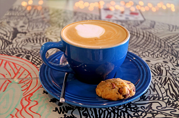 Tazza di caffè cappuccino con un biscotto al cioccolato isolato sul tavolo - Foto, immagini