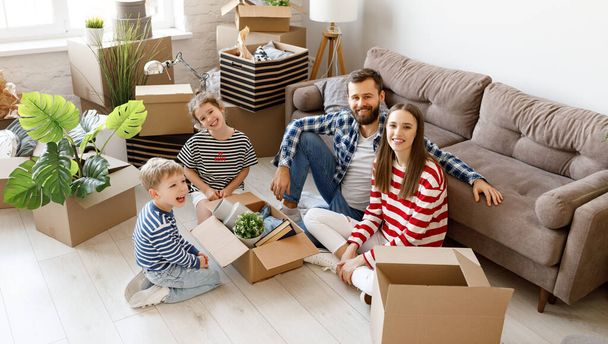 Z výše šťastné rodiny sedící na podlaze v blízkosti kartonových krabic a vybalování vázy při stěhování v novém bytě - Fotografie, Obrázek