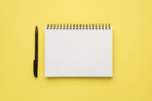 Foto sopraelevata di notebook e penna nera isolata sullo sfondo giallo - Foto, immagini
