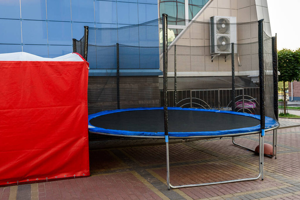 Sininen trampoliini lapsille lähellä rakennusta kaupungissa. - Valokuva, kuva