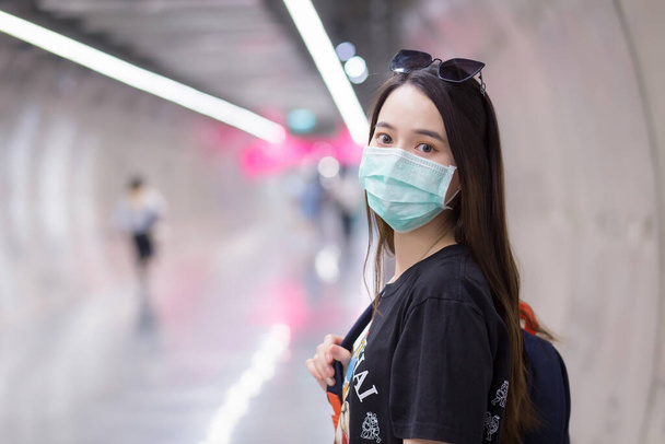Aasialainen kaunis nainen pukeutuu musta paita ja lääketieteellinen kasvonaamio, kun hän kävelee Subway tunneli ja pitää reppu käsissään. terveydenhuolto, saastuminen PM2,5 ja uusi normaali käsite. - Valokuva, kuva