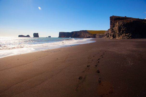 Schwarzer Sand am Strand von Reynisfjara in Island. Felsen und Klippen am Meeresstrand bei Sonnenuntergang. Ein beliebter Touristenort an der Südküste Islands. - Foto, Bild
