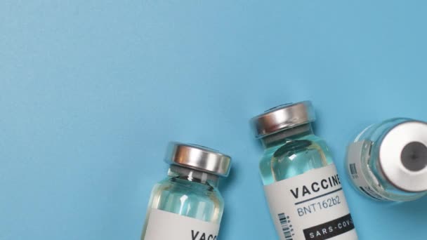 Fiolki ze szczepionką lub butelki ze szczepionką przeciwko koronawirusowi na niebieskim tle. Szczepienie, wstrzyknięcie, badanie kliniczne - Materiał filmowy, wideo
