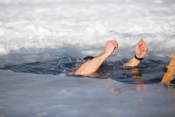 Ένας άνθρωπος βυθίζεται σε μια τρύπα πάγου κατά τη διάρκεια της χειμερινής γιορτής του βαπτίσματος του Ιησού. Ένας άντρας κολυμπάει στην τρύπα του πάγου το χειμώνα. Θαλάσσιοι ίπποι. - Φωτογραφία, εικόνα