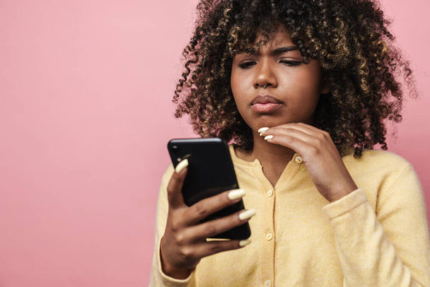 Ampollante mujer afroamericana usando teléfono móvil aislado sobre pared rosa - Foto, imagen