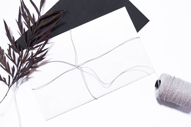 Carta bianca su busta nera con foglia secca e spago. Natura morta composizione su sfondo bianco. - Foto, immagini