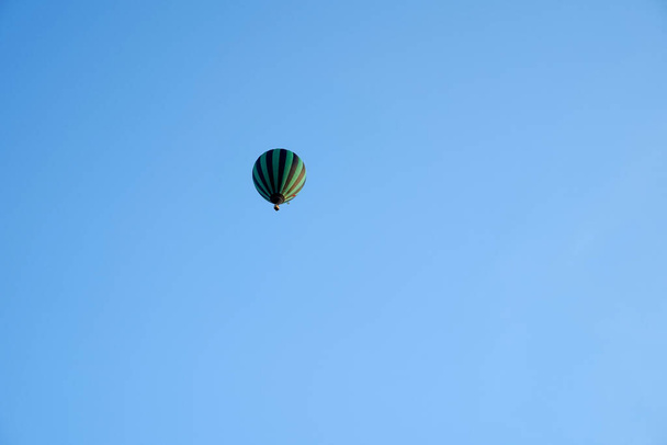 Μαύρο και πράσινο αερόστατο θερμού αέρα ψηλά σε ένα μπλε ουρανό - Φωτογραφία, εικόνα