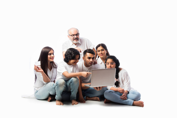 Πολυεθνική ινδική ασιατική οικογένεια έξι online αγορών χρησιμοποιώντας φορητό υπολογιστή και ηλεκτρονική κάρτα, ενώ κάθεται σε λευκό φόντο - Φωτογραφία, εικόνα